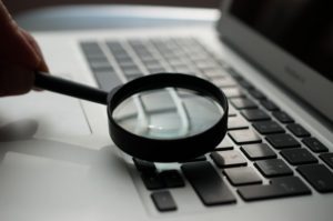 A photograph of a hand holding a black magnifying glass over the keyboard of a laptop.