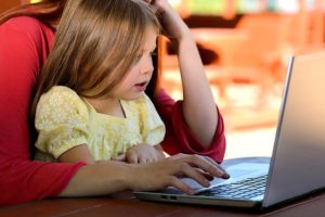 This is a photo of a child sitting on the lap of an adult as the adult navigates the laptop open before them both.