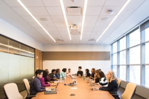 This is a photograph of a conference room filled with people sitting at a table exchanging ideas.