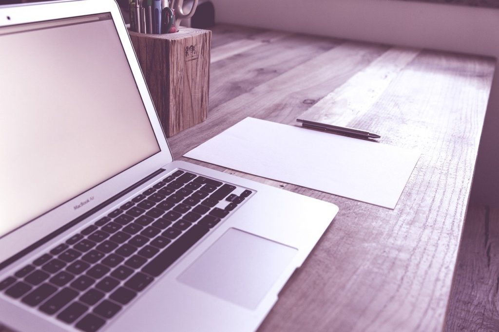 This is an angled, side-view photograph of an open laptop sitting on a wooden desk.