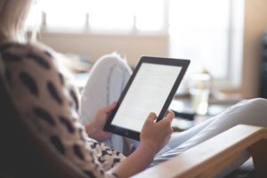 This is an over-the-shoulder photo of a person sitting back on a chair and reading on a Kindle.