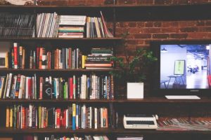 This is a photo shelves of books next to a large monitor, keyboard, and a typewriter to exemplify an eLearning experience with WordPress and LMS.