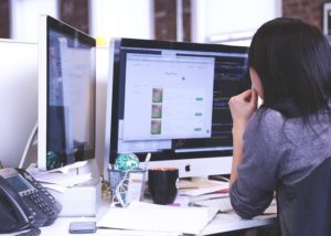 This is a photo taken from behind a remote worker who is looking at the monitor of her desktop computer.