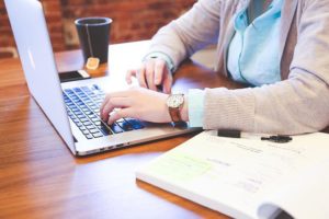 This is an image of student on a laptop with an open book nearby and a beverage.