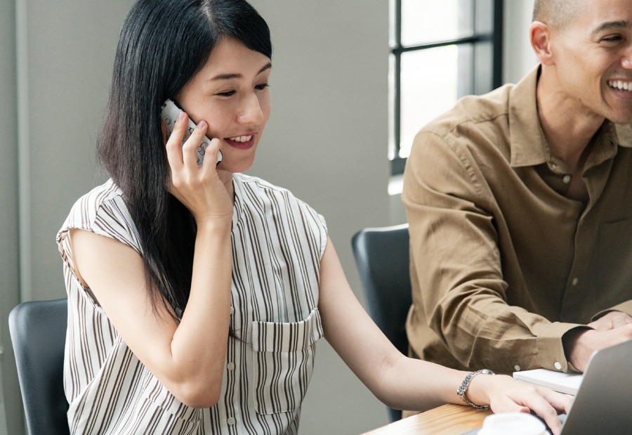 Photograph of a woman on a telephone as she sits at a desk next to her smiling coworker used for a blog post titled "Web Design and Development Myths 2019 Edition."