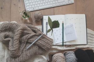 This is a photograph of an unfinished knitting project sitting next to a journal and some hand drawn sketches on top of a wooden desk.